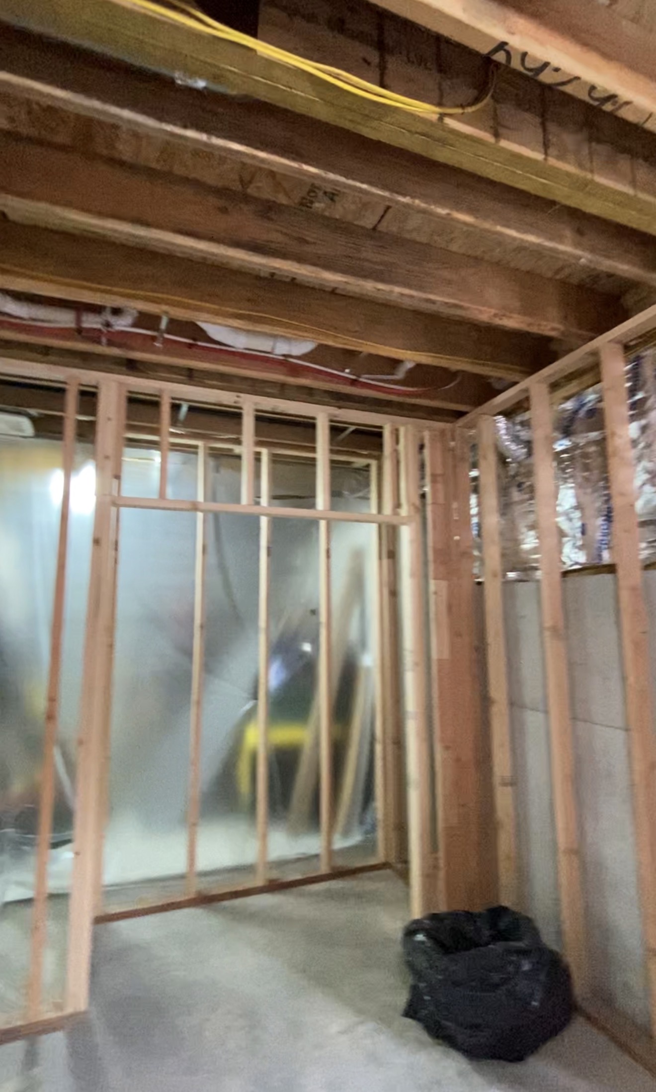 New basement walls framed against the foundation, with joists, wiring and insulation exposed above