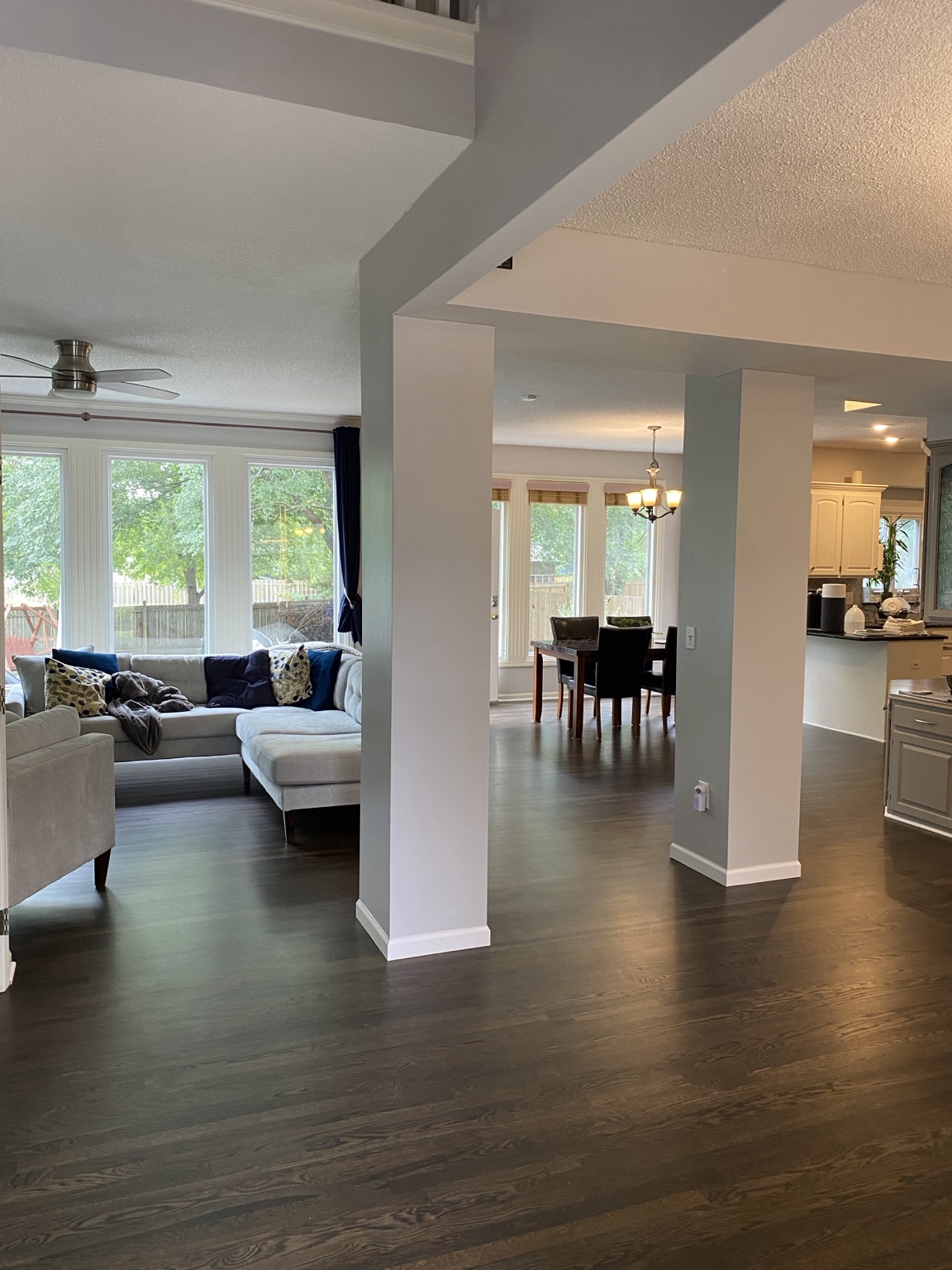Completed open main floor with framed structural openings and columns connecting the living room, dining area and kitchen over continuous dark hardwood flooring