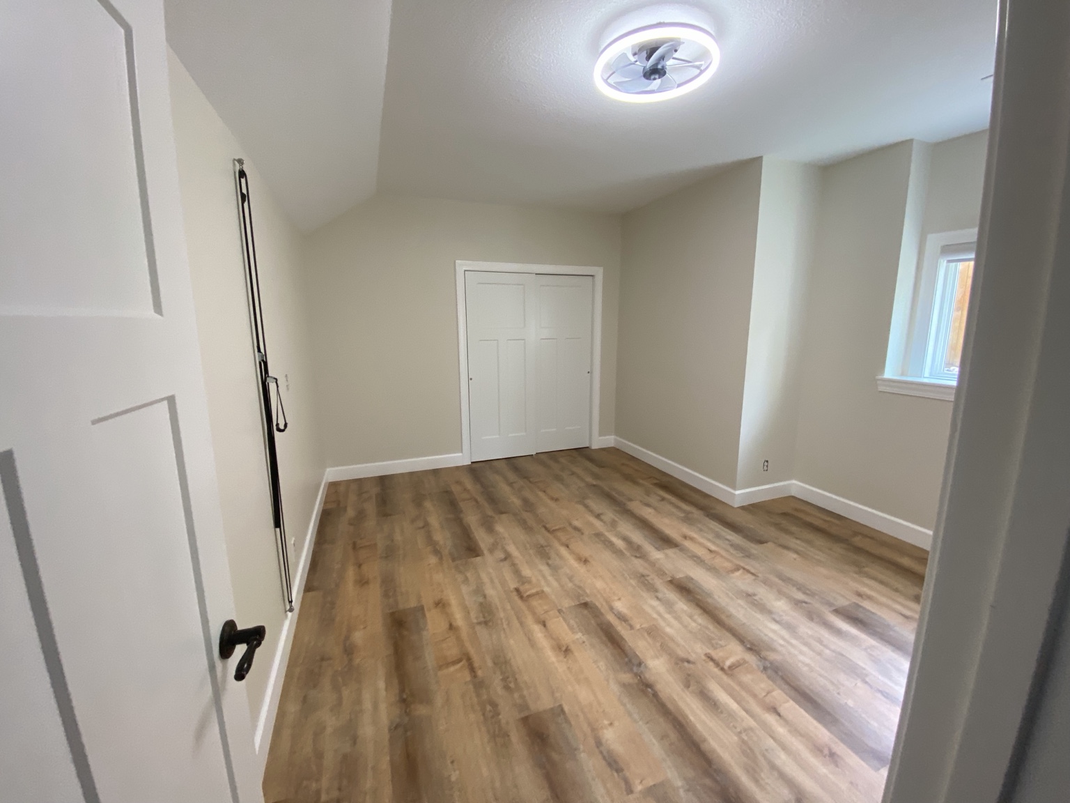 Completed room before furnishing, with warm greige walls, wood-look flooring, white closet doors and a ceiling fan light