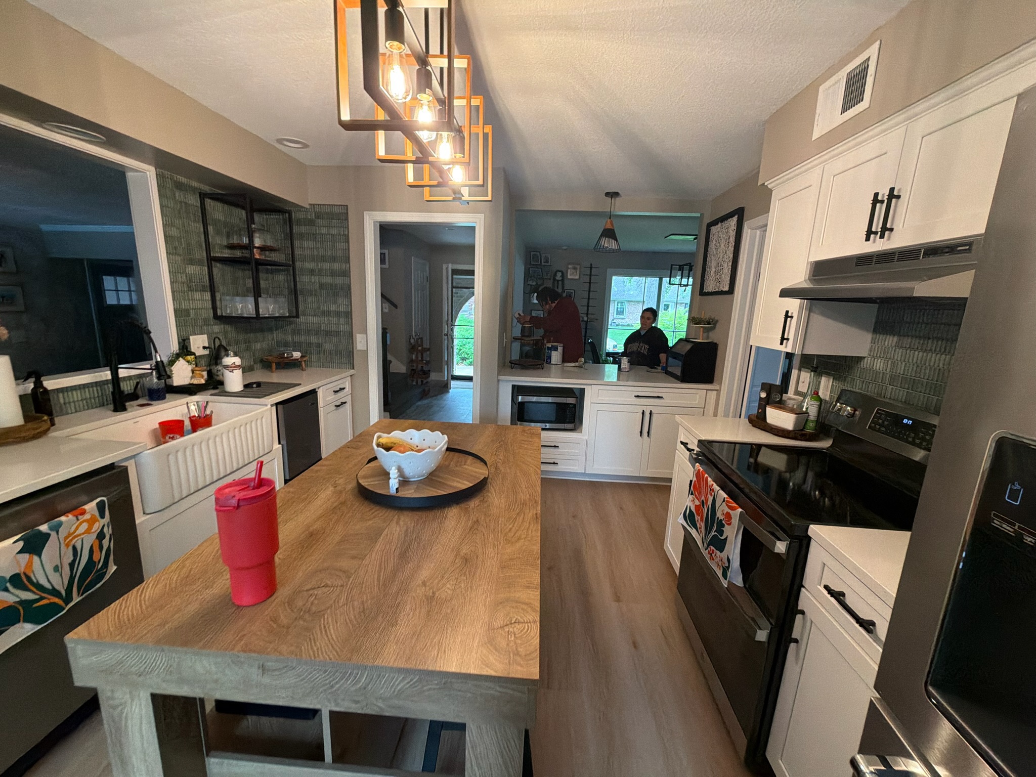 Completed kitchen with farmhouse sink, green tile backsplash and the island in the foreground