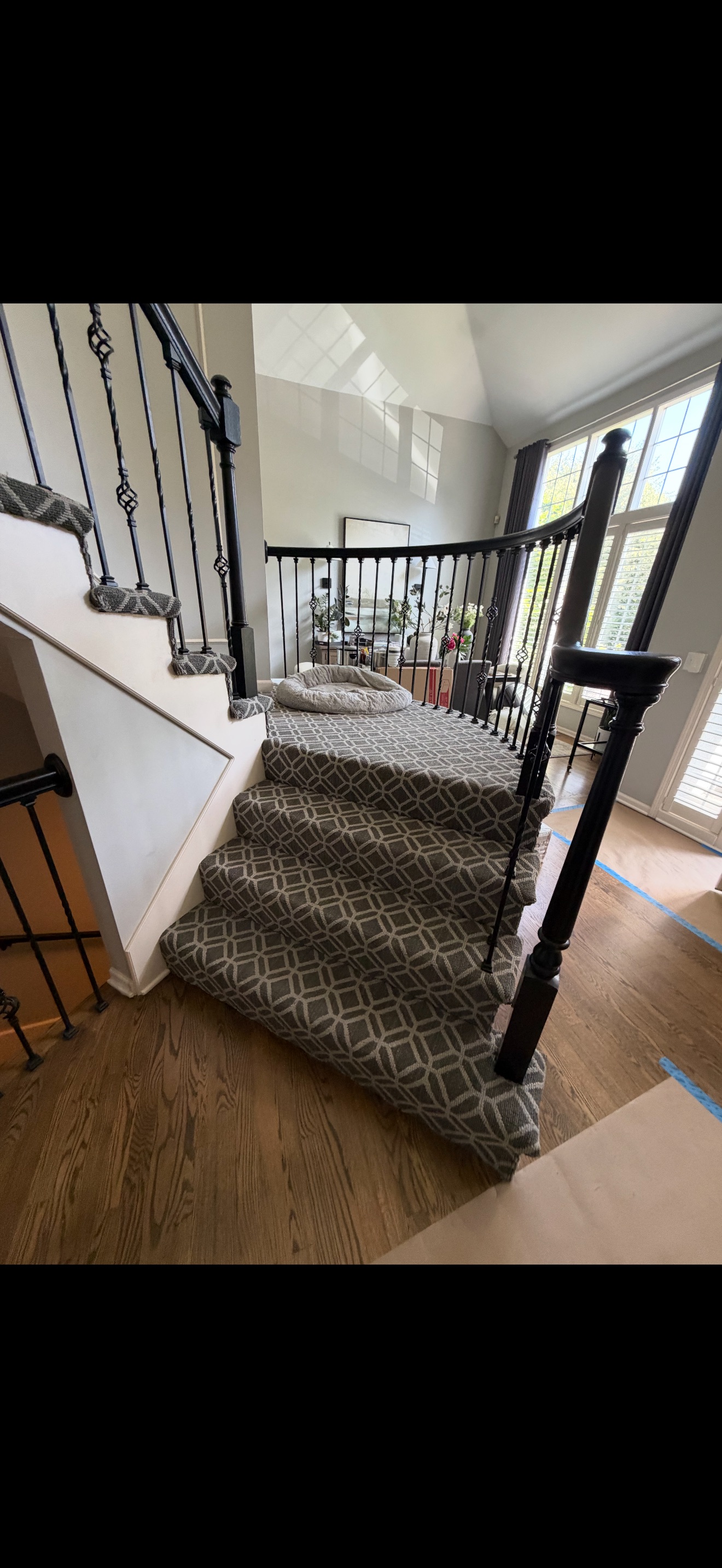 Staircase before the work, fully carpeted with patterned carpet over the treads and a dark railing