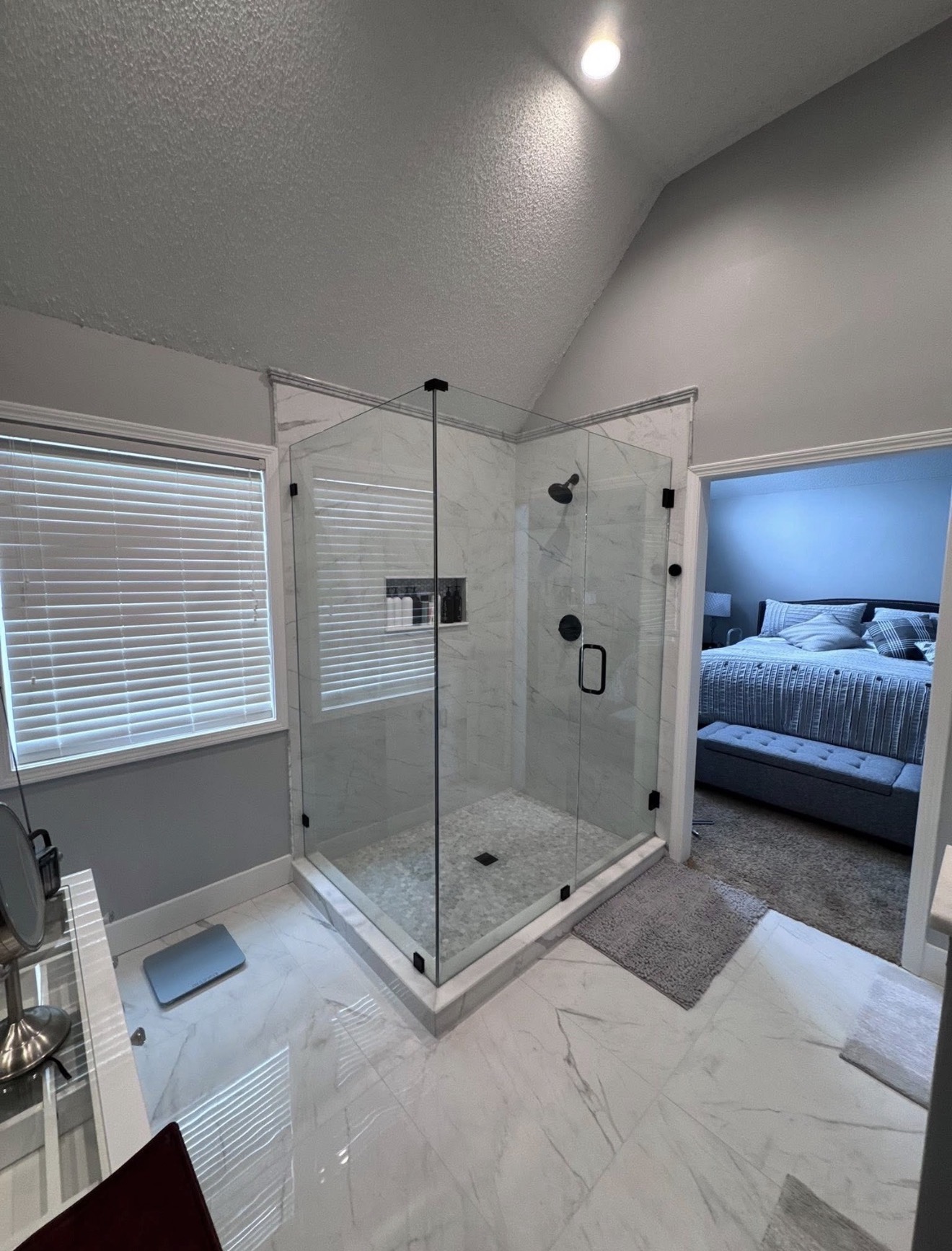Completed primary bathroom with a glass-enclosed custom shower and the adjoining bedroom visible through the opened layout