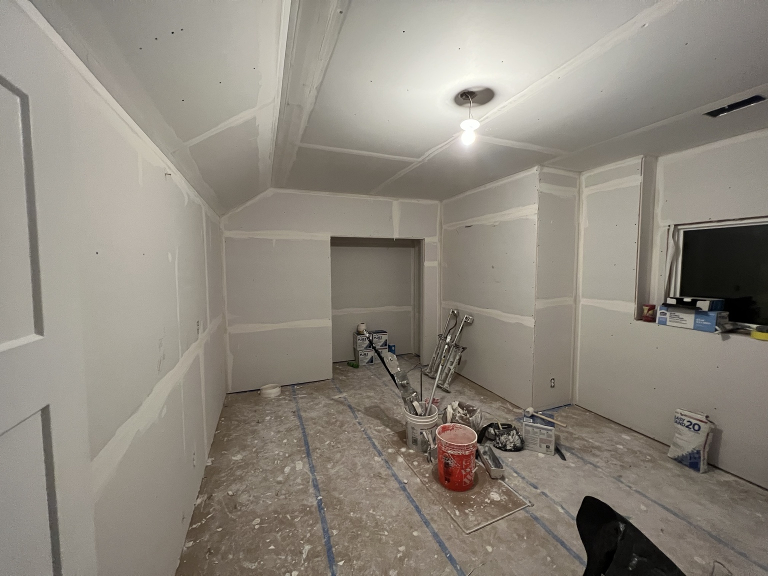 The same basement room at the drywall stage, hung and taped with compound and tools still on the floor