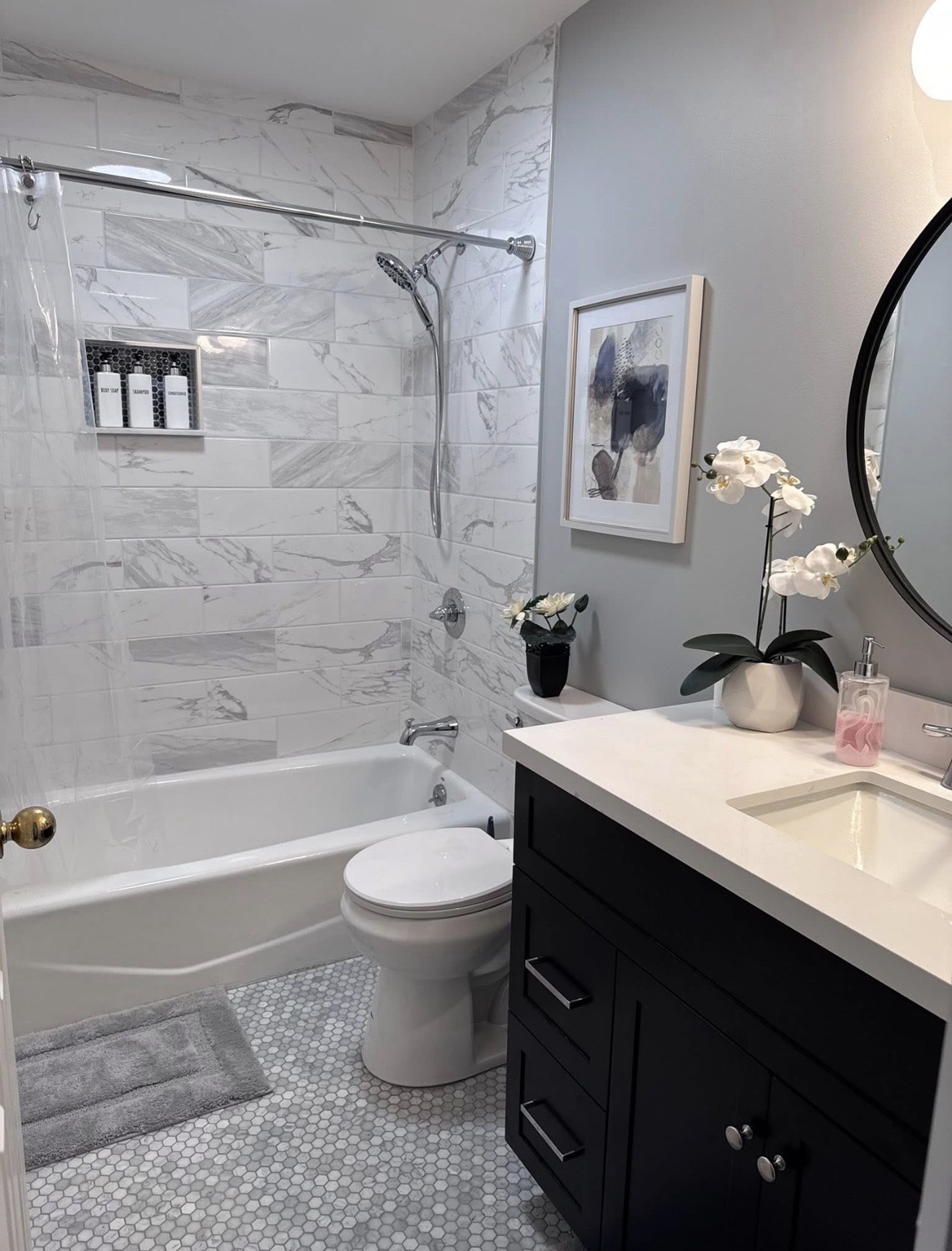 Completed secondary bathroom with a tiled tub and shower surround, a recessed niche, small hex tile floor, and a black vanity with a white countertop