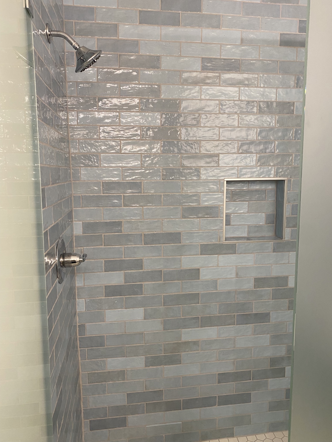 Inside the finished shower, tiled floor to ceiling in variegated blue-grey glazed tile with a recessed niche and brushed-nickel fixtures