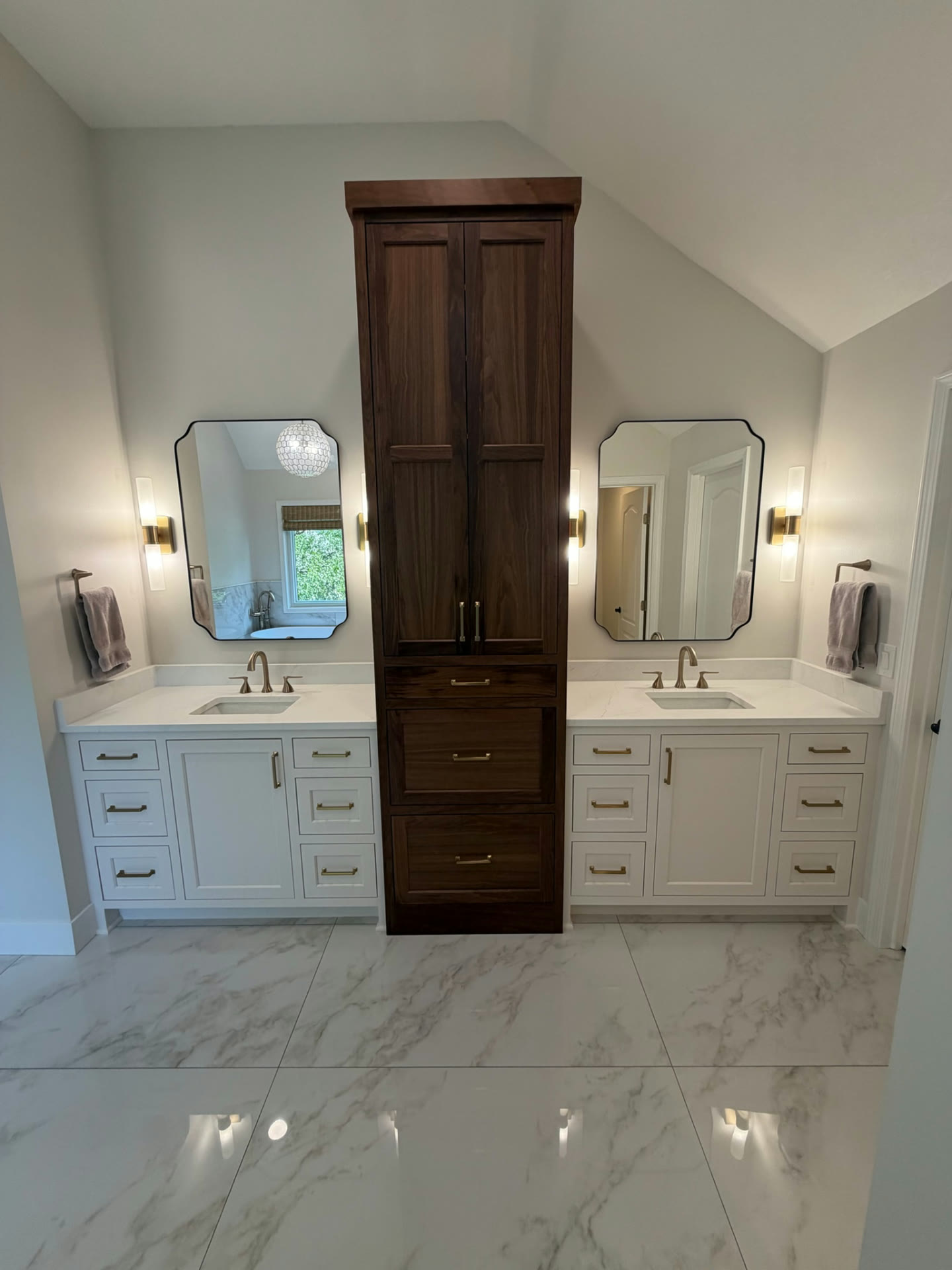 Completed double vanity with white cabinetry, stone countertops and a walnut storage tower between two mirrors