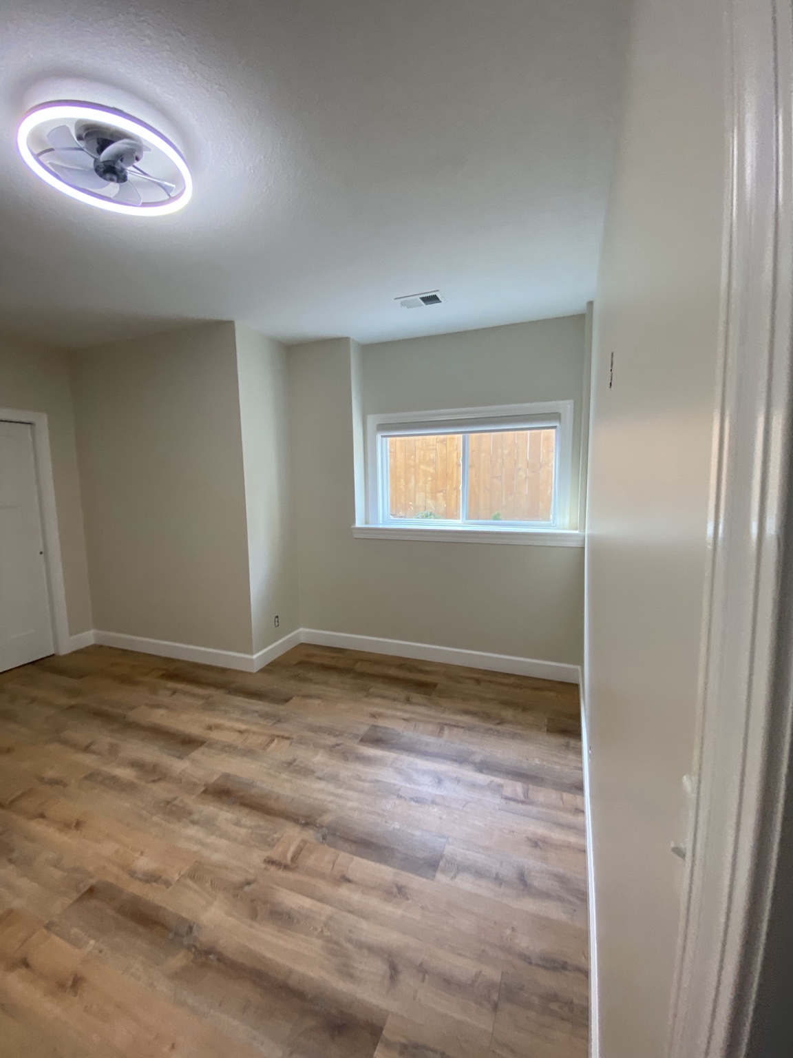 Completed room looking toward the egress window, with new trim, baseboards and wood-look flooring