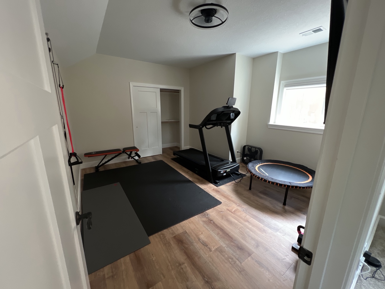 Completed room set up as a home gym with treadmill, floor mats, rebounder and wall-mounted training straps