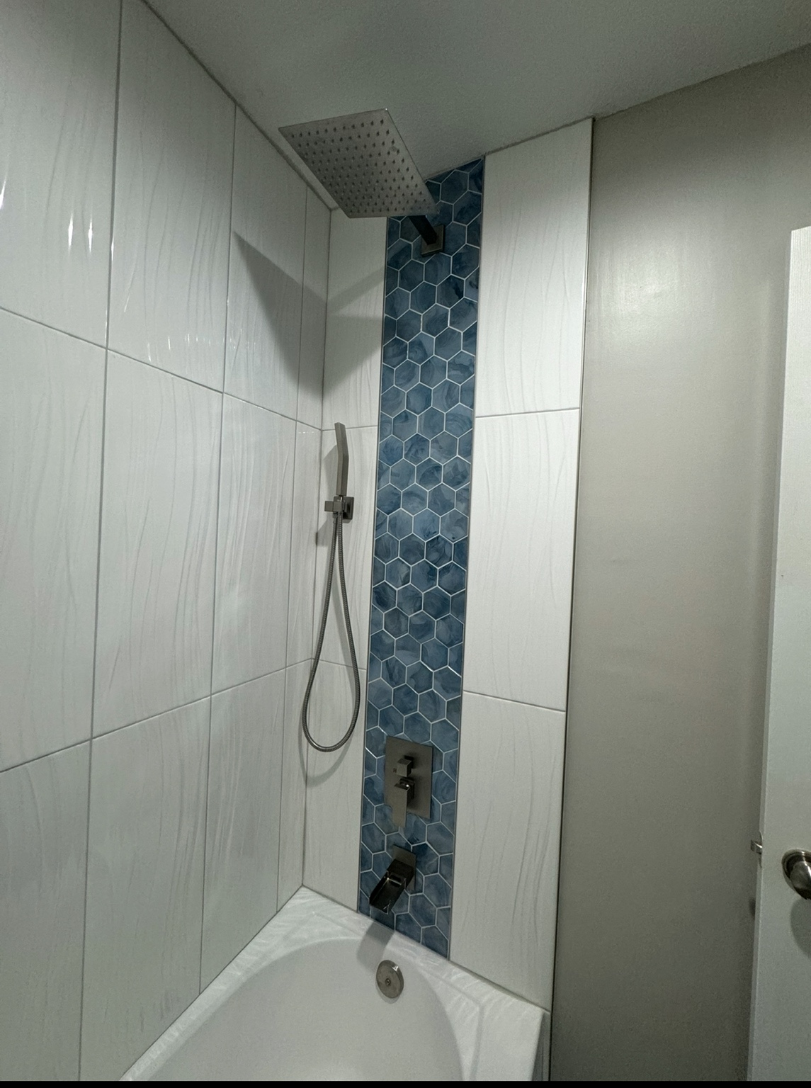 Shower fittings against the blue hexagon accent band running the full height of the white tiled surround
