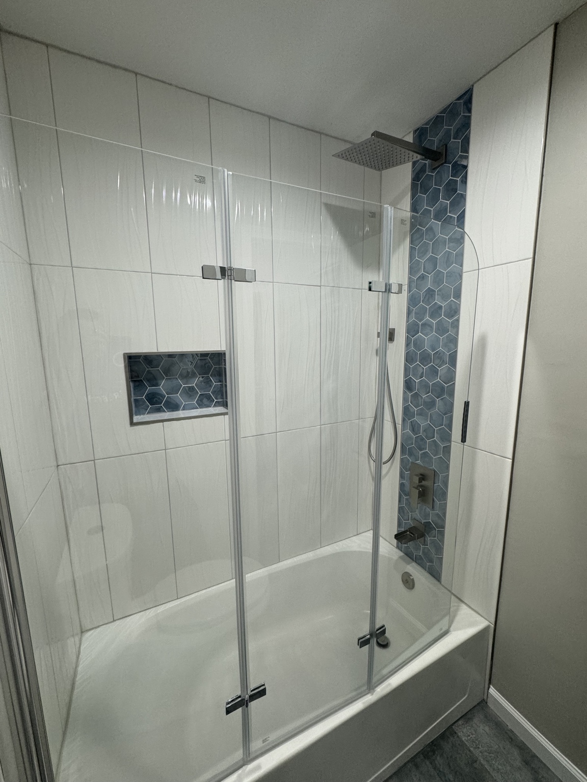 Tiled tub and shower surround with a blue hexagon accent band, a matching tiled niche and a folding glass enclosure