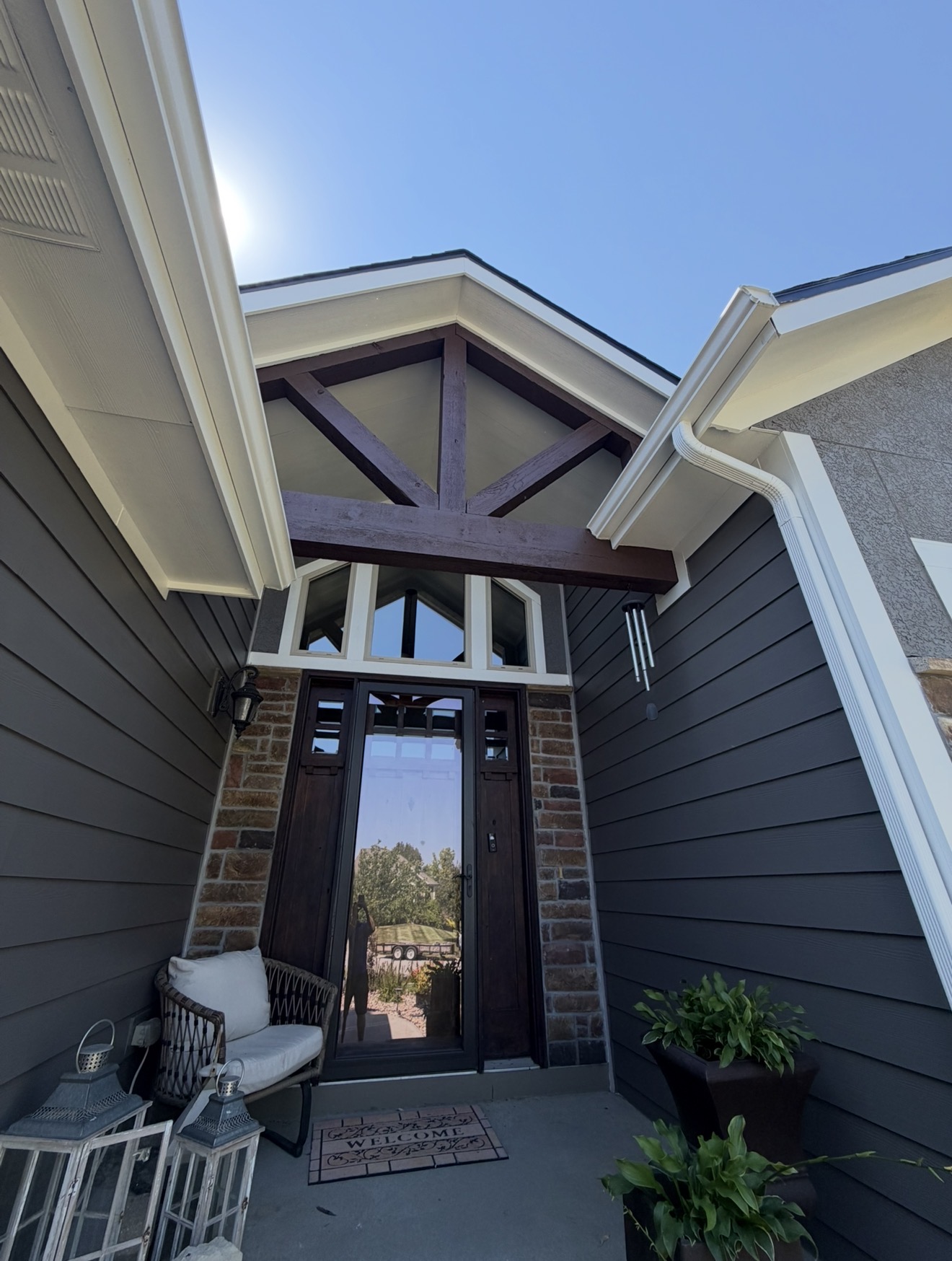 Completed covered entry with stained timber truss, dark front door, brick columns and deep charcoal siding with white trim