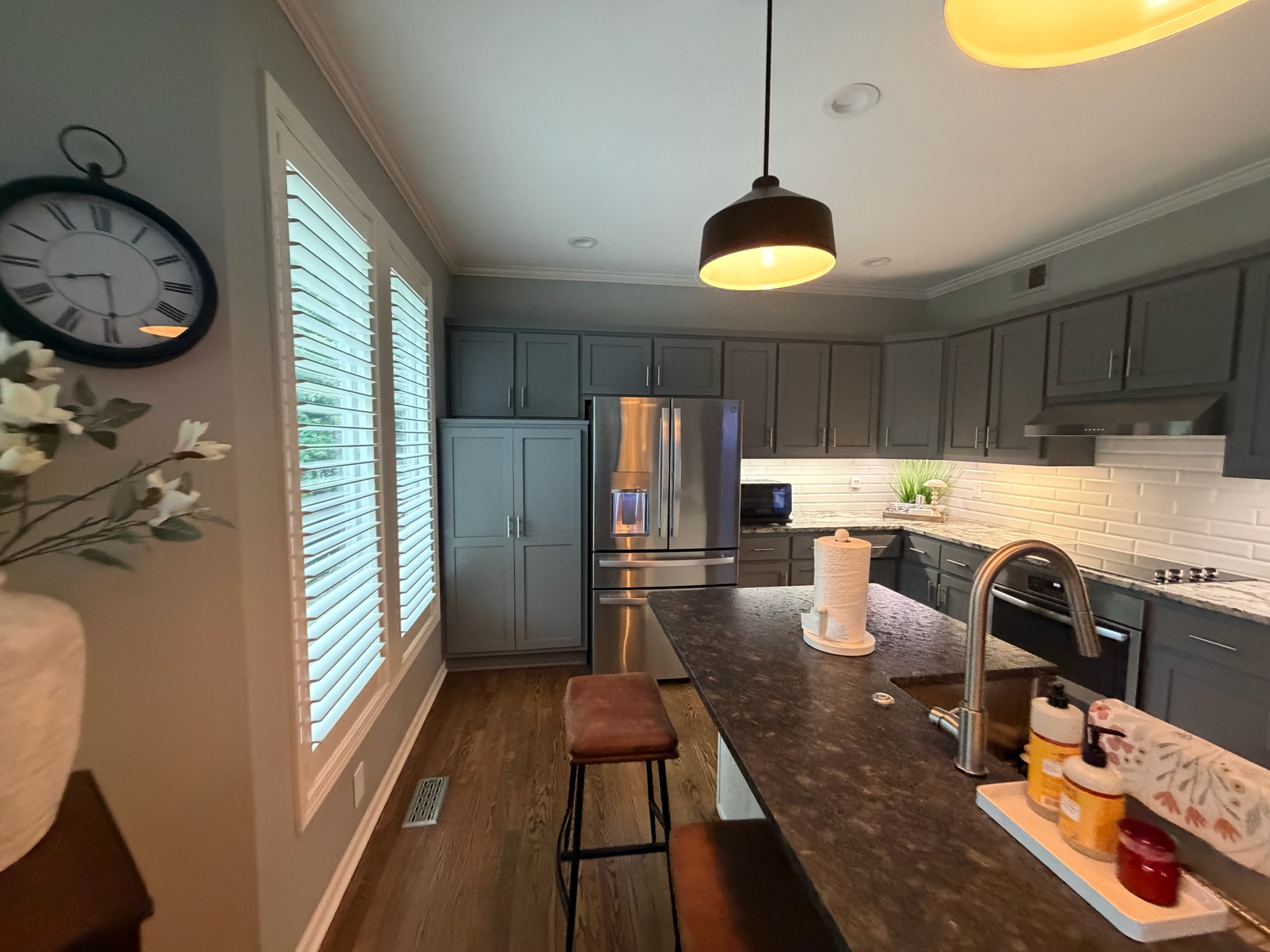 Original darker cabinetry along the refrigerator and pantry wall before refinishing, with the existing countertops and backsplash in place