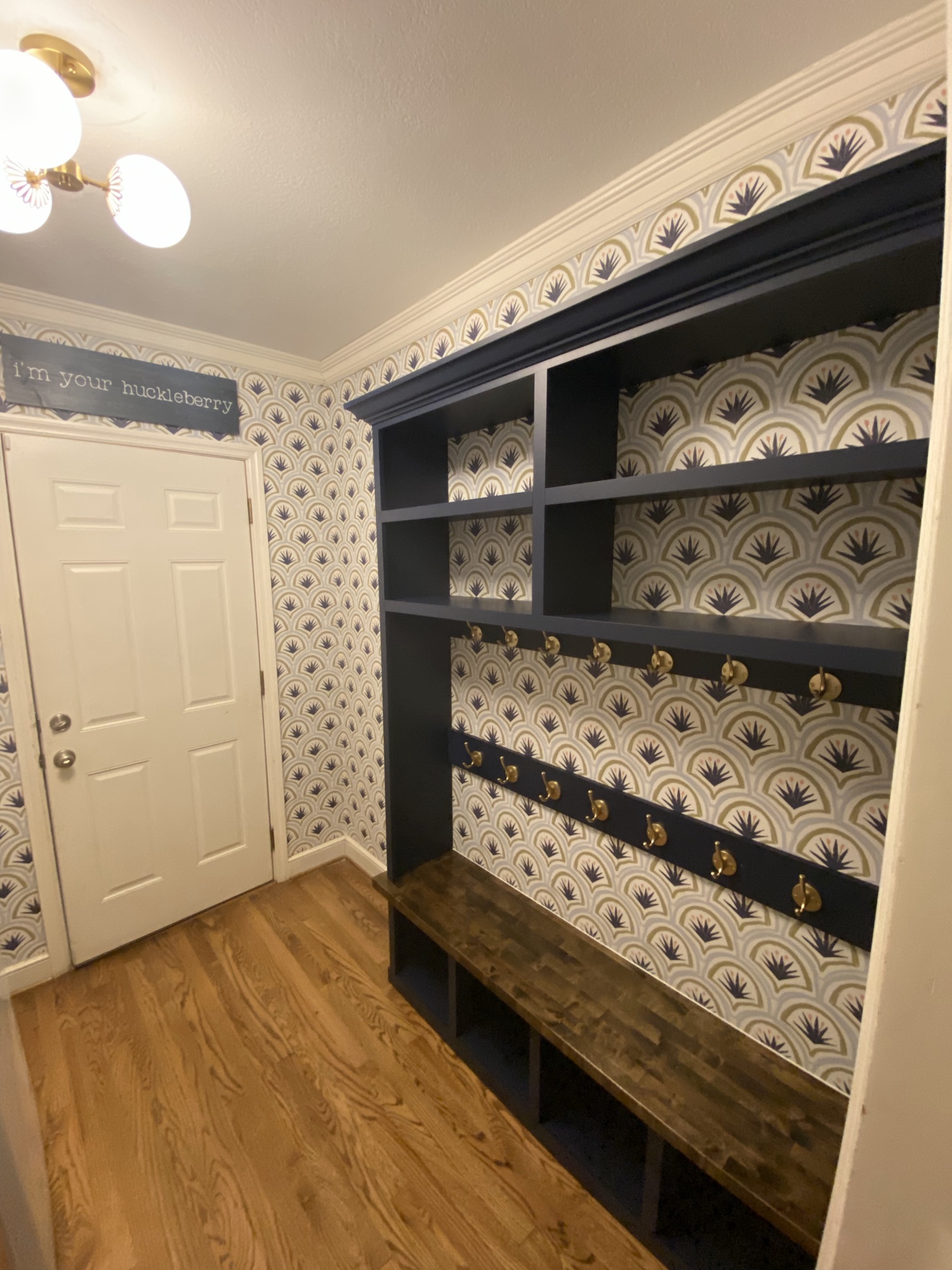 Angled view of the completed mudroom built-in with open shelving, hooks and bench storage below